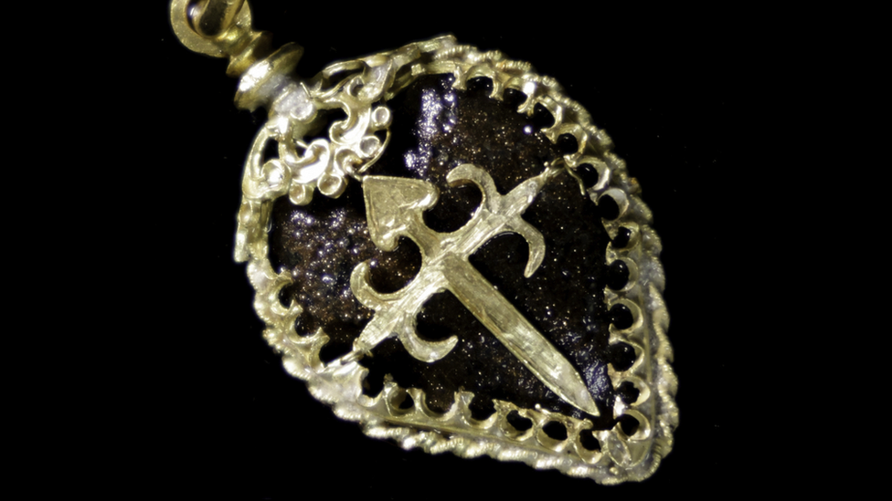A gold earring with the cross of Santiago in the centre