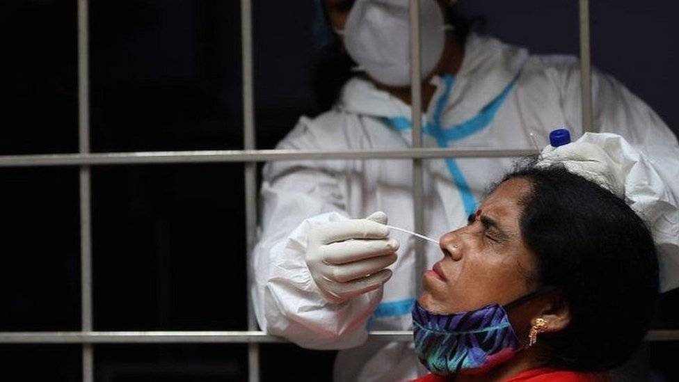 Um trabalhador de saúde coleta uma amostra de esfregaço de uma mulher em Delhi