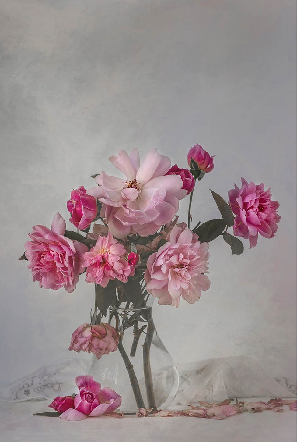 Увядшие розовые розы в вазе с льняными салфетками на столе
