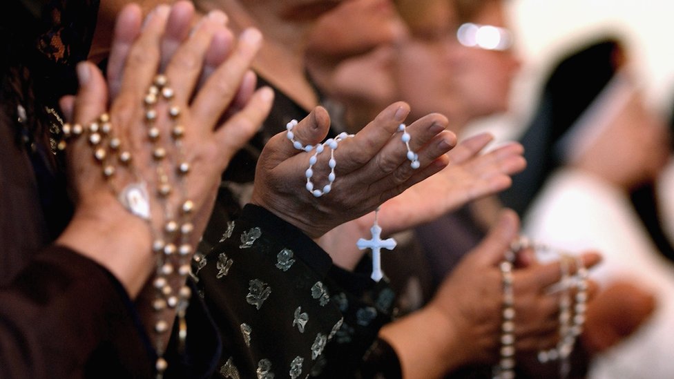 Personas rezando con rosarios.