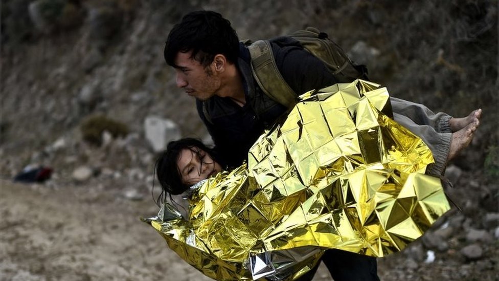 Мужчина несет девушку, когда беженцы и мигранты прибывают на греческий остров Лесбос после пересечения Эгейского моря из Турции 1 октября 2015 года.