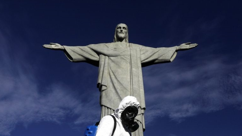 Homem todo coberto pro trajes sanitários em frente à estátua do Cristo Redentor