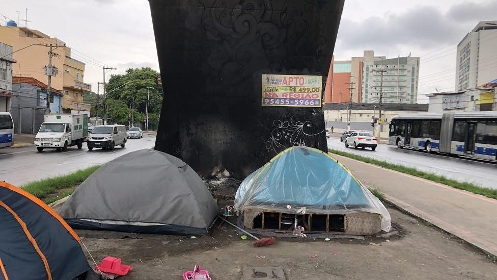 3 barracas em frente a uma pilastra de viaduto