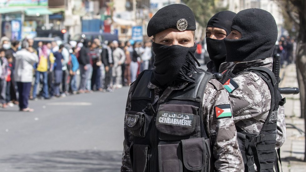 Силы безопасности Иордании наблюдают, как люди стоят в очереди за хлебом в Аммане (24 марта 2020 г.)