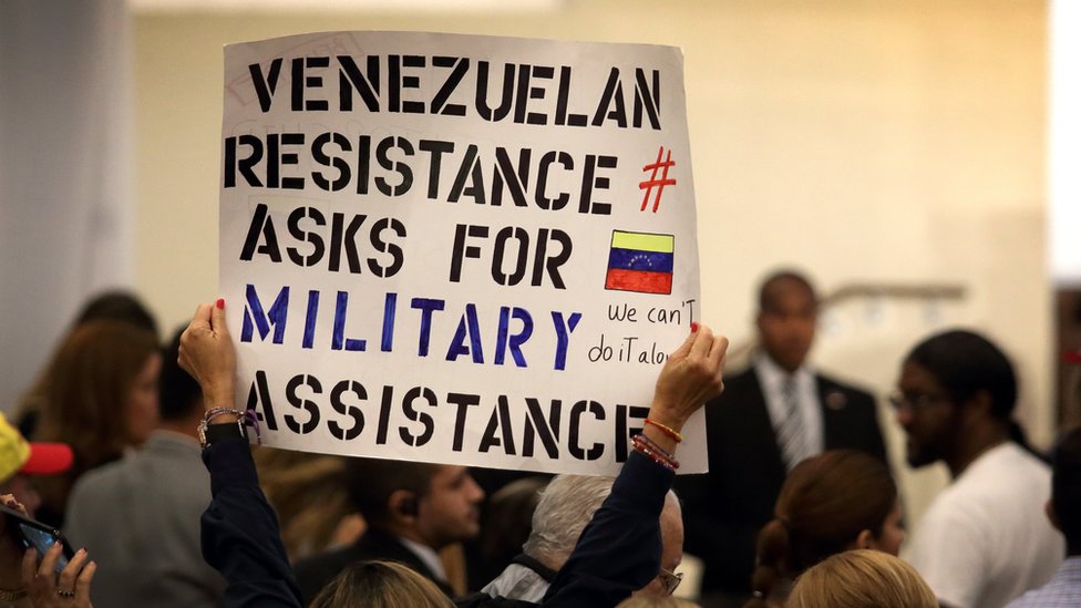 Algunos venezolanos mostraban carteles pidiendo "ayuda militar" para la situación de Venezuela. Una mujer sostiene un cartel en la reunión de venezolanos con Mike Pence