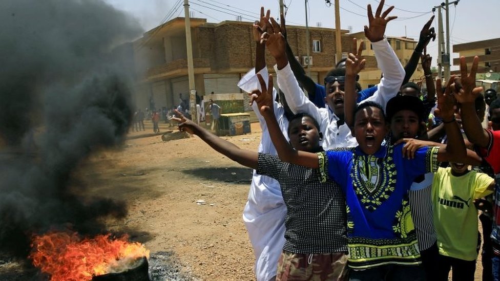 Суданские протестующие жестикулируют и выкрикивают лозунги на баррикаде вдоль улицы, требуя, чтобы Переходный военный совет страны передал власть гражданским лицам, в Хартуме, Судан, 5 июня 2019 года