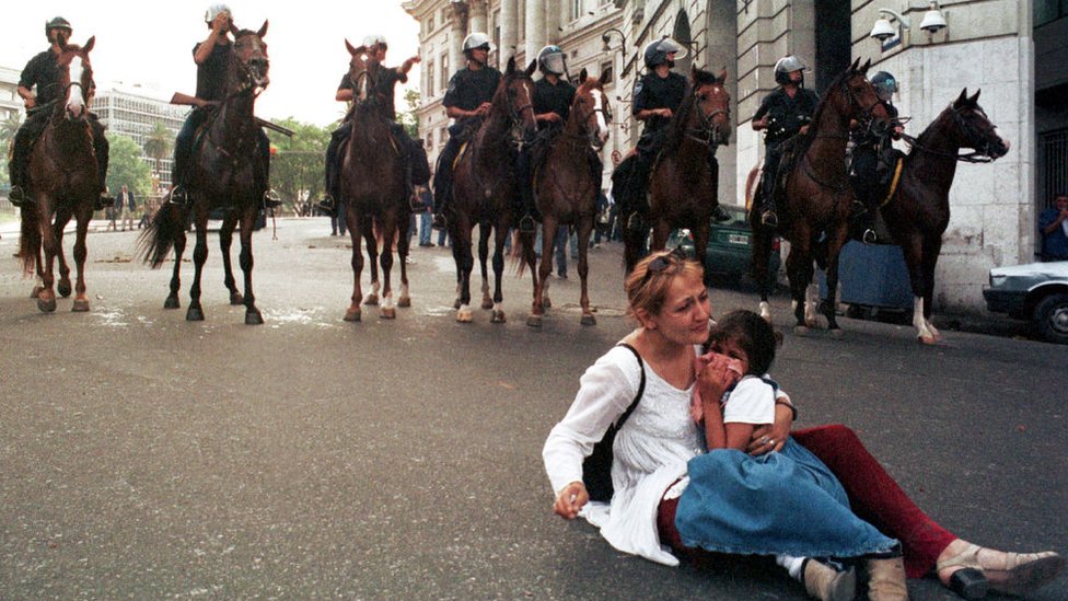 Una mujer con una niña en las inmediaciones de Plaza de Mayo con caballos de la policía detrás.