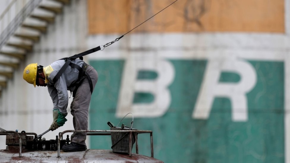 Operário agachado e trabalhando em frente a logo da Petrobras pintado no muro