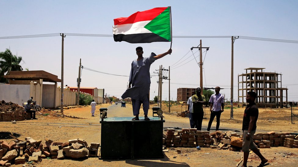 Суданский протестующий держит национальный флаг, стоя на баррикаде вдоль улицы, требуя, чтобы Переходный военный совет страны передал власть гражданским лицам, в Хартуме, Судан, 5 июня 2019 г.