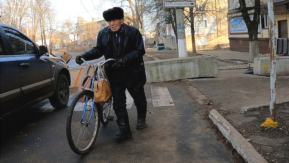 Stariji muškarac gura bicikl na ulici u Bahmutu
