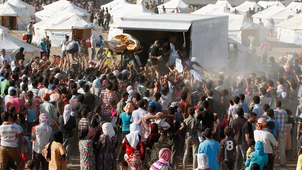 عدد من اللاجئين يتوافدون على سيارة مساعدات في أحد المخيمات