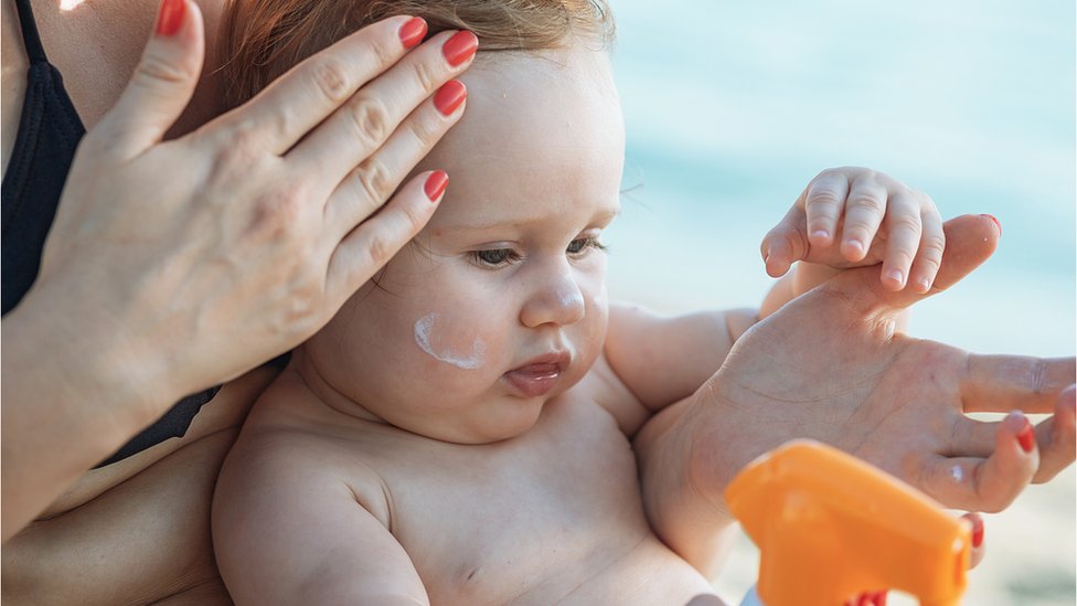 Мама наносит солнцезащитный крем на ребенка