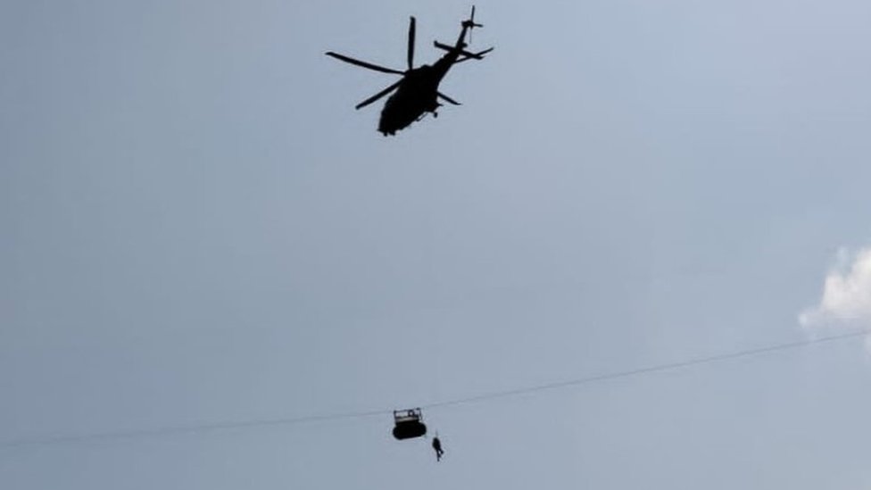 A military helicopter hovers above the stranded cable car