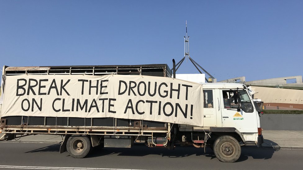 Мимо парламента проезжает грузовик с большой табличкой на боку: «Прекратите засуху с помощью действий по борьбе с изменением климата!»