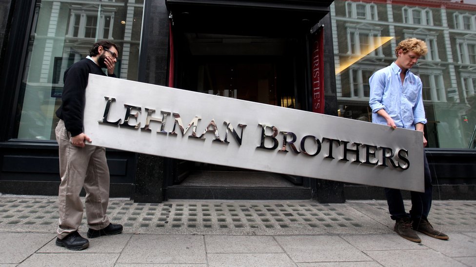 Dos hombres en una subasta portando un cartel de Lehman Brothers