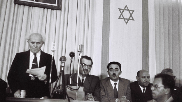 David Ben Gurion Standing alongside the Star of David reading from a piece of paper