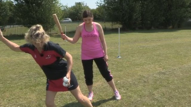 trainer showing a woman the correct stance for batting in rounders