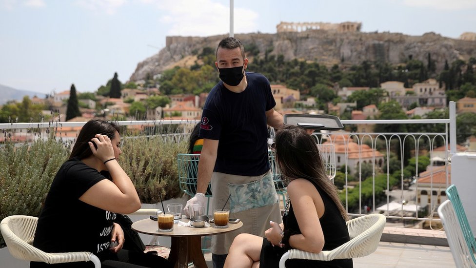 A waiter wearing a protective face mask serves customers in a coffee shop, with the Acropolis hill in the background, as restaurants reopen following the easing of measures against the spread of the coronavirus disease (COVID-19), in Athens, Greece