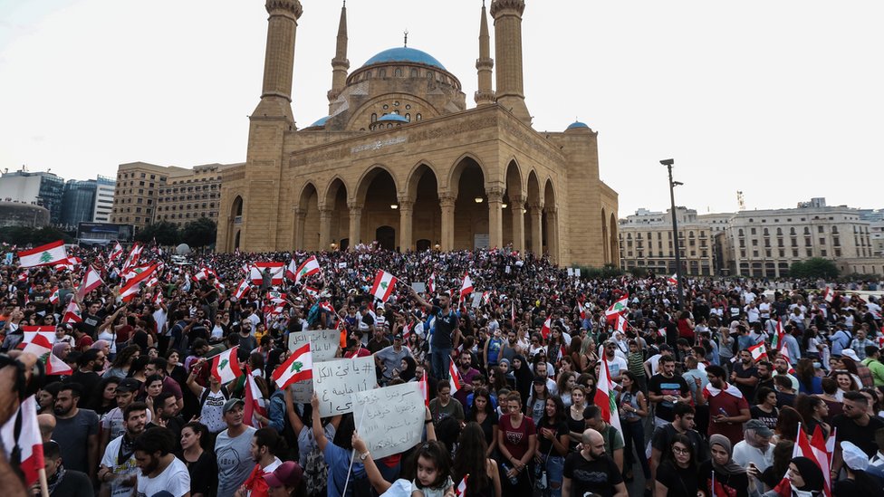 Протестующие размахивают ливанскими флагами и выкрикивают антиправительственные лозунги перед правительственным дворцом в центре Бейрута, Ливан (19 октября 2019 г.)