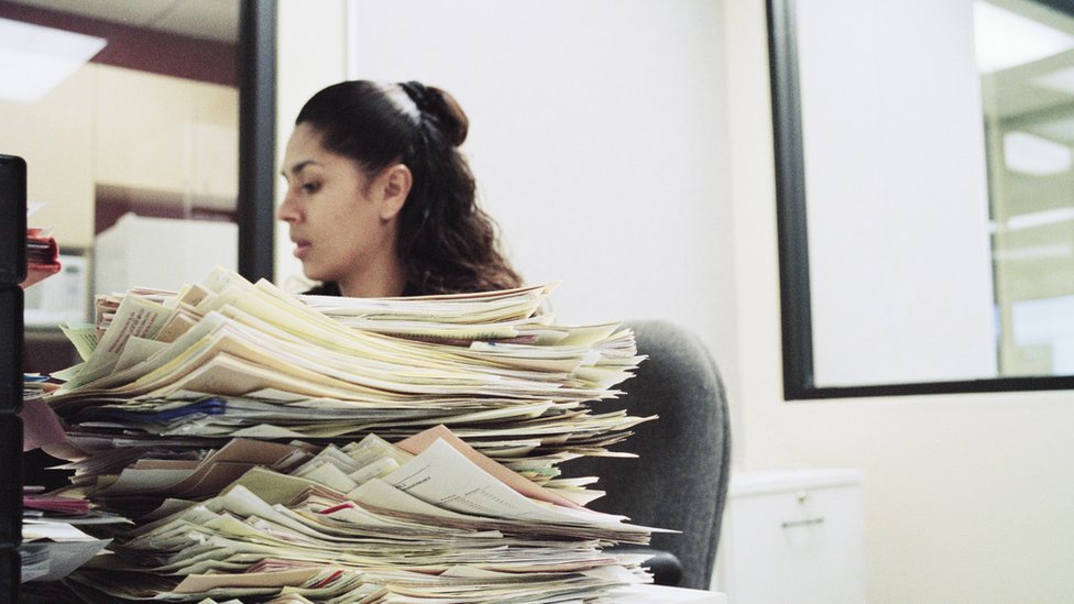 Mulher no escritório com mesa cheia de documentos