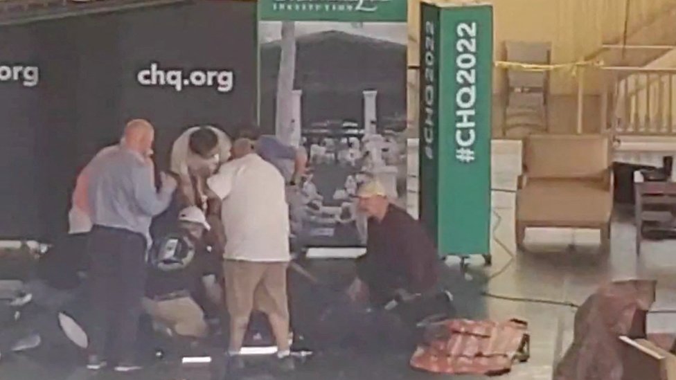 Fotografia com má resolução mostra pessoas em um palco ajudando uma pessoa caída no chão