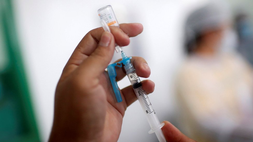 Close na mão de um profissional de saúde enchendo uma seringa com vacina