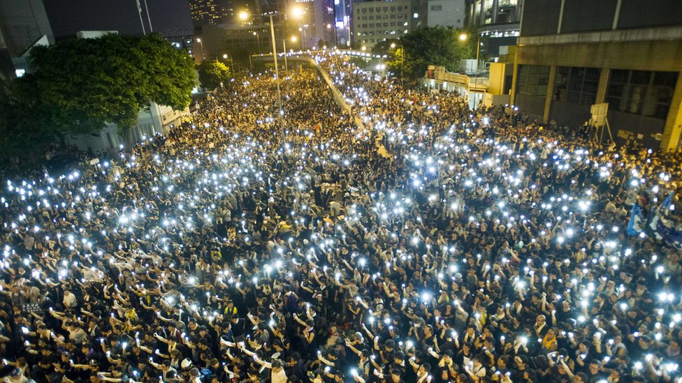 Протестующие и студенты-демонстранты держат свои мобильные телефоны в знак солидарности во время акции протеста у здания Законодательного совета в Гонконге 29 сентября 2014 г.