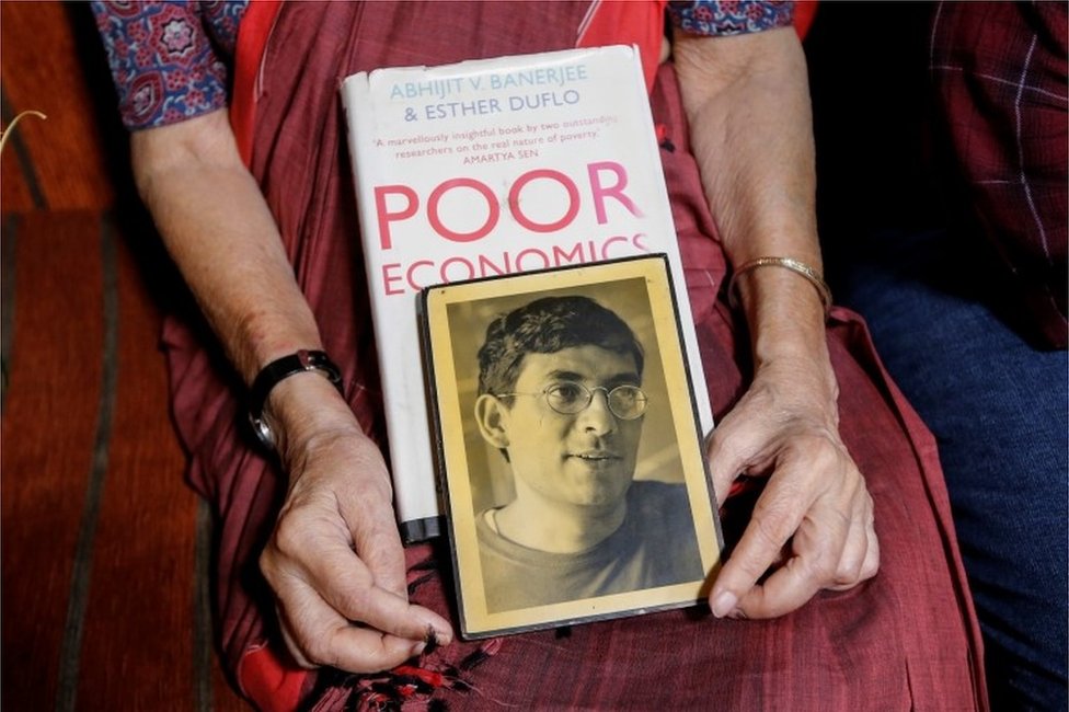 Нирмала Банерджи, мать Абхиджита Банерджи, одного из лауреатов Нобелевской премии по экономике 2019 года, держит его портрет и одну из его книг, когда она разговаривает со СМИ в своем доме в Калькутте, Индия, 14 октября 2019 года.