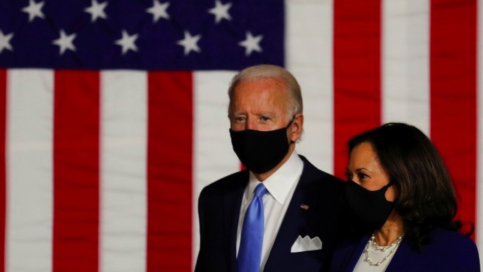Joe Biden and Kamala Harris wearing masks in front of a Stars and Stripes flag