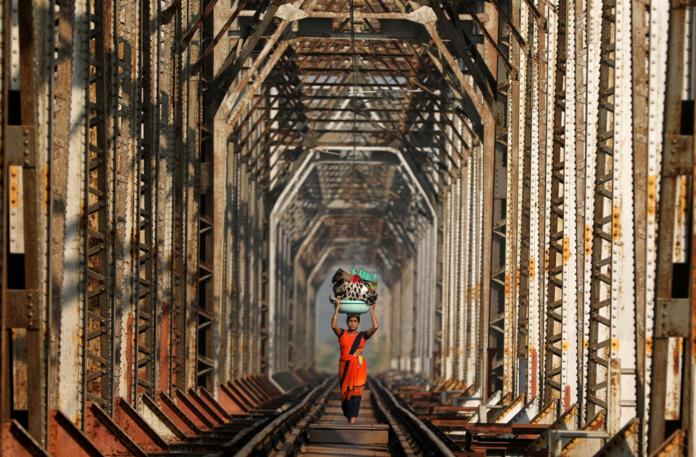 A woman carries luggage along a railway track