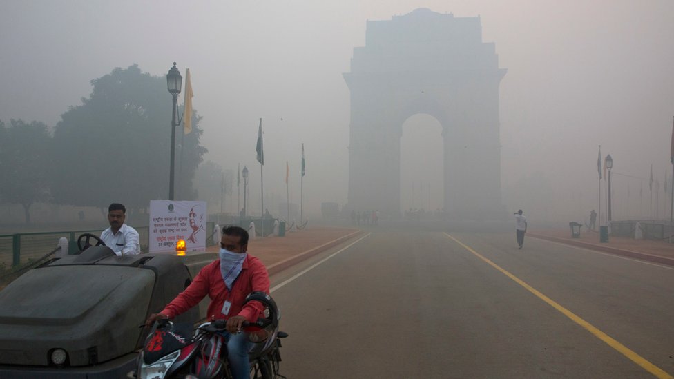 Утром после фестиваля Дивали в Нью-Дели мужчина закрывает лицо шарфом, проезжая мимо знаменитых ворот Индии, окутанных дымом и смогом