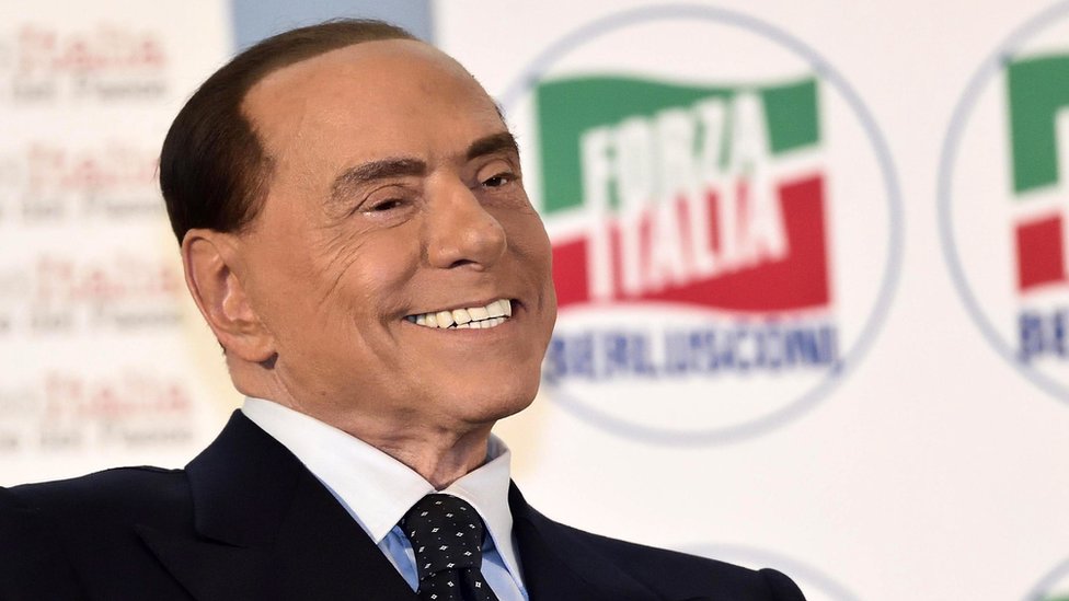 Silvio Berlusconi pictured smiling at a political event in 2017. He is pictured here with a Forza Italia logo visible behind him.