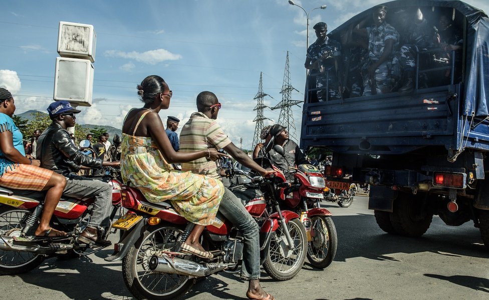 Люди едут на мотоциклах за грузовиком, перевозящим силы безопасности в Бужумбуре 15 мая 2015 года