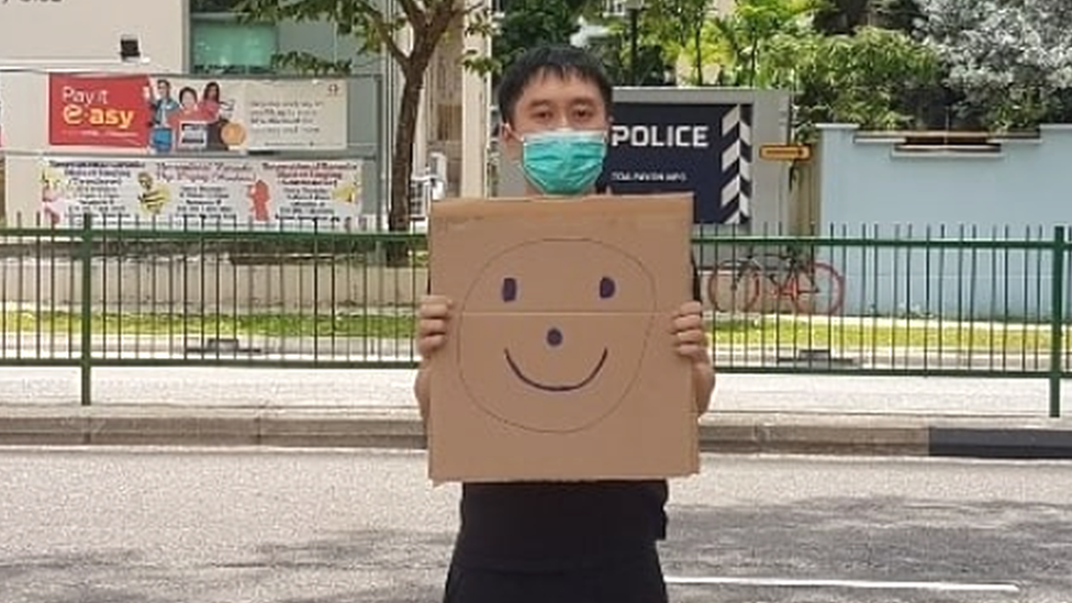范國瀚在新加坡大巴窯鄰里警局外舉起畫上笑臉的紙皮（范國瀚提供照片28/3/2020）