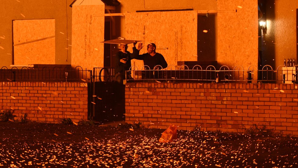 Двое мужчин укрываются от углей, вылетающих из костра на площади Хоупвелл в районе Шанкилл в Белфасте
