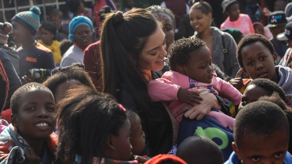 Мисс Южная Африка держит чернокожего ребенка без перчаток