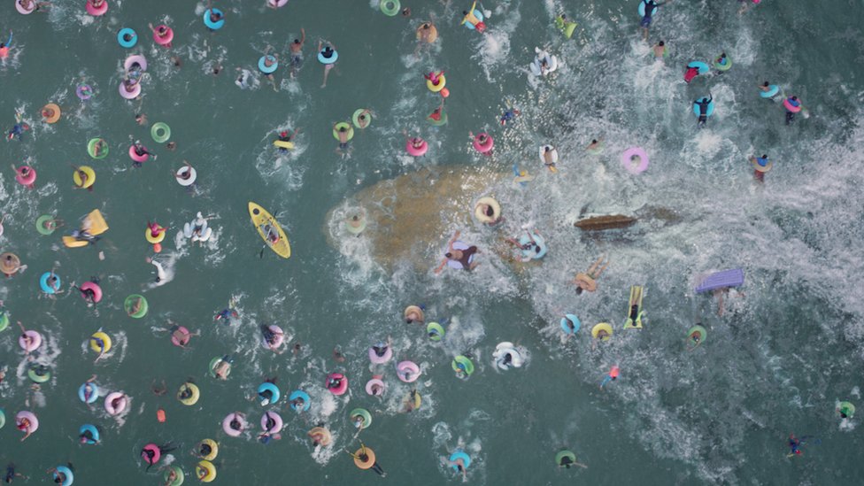 Escena de la película Megalodón, donde un tiburón nada por debajo de bañistas en flotadores en el mar.