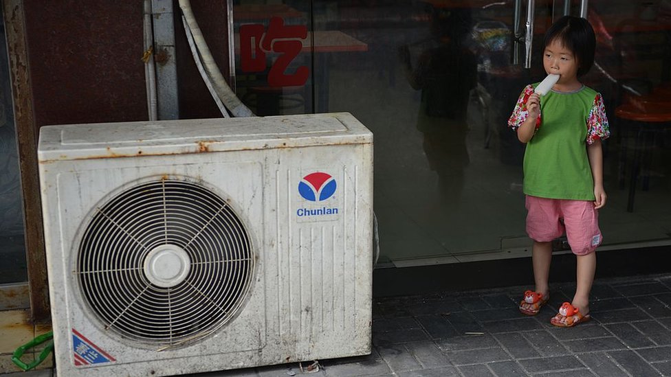 A young girl eats an ice lolly next to an air conditioning unit in Shanghai