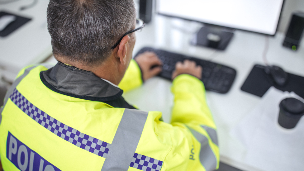 One senior traffic warden sitting at the office in front of the computer and writing a report