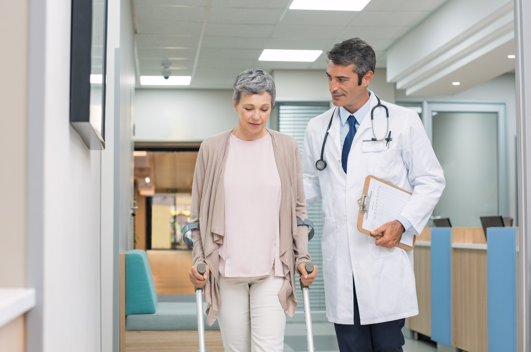 Una mujer con una fractura trata de caminar con muletas junto a un médico.