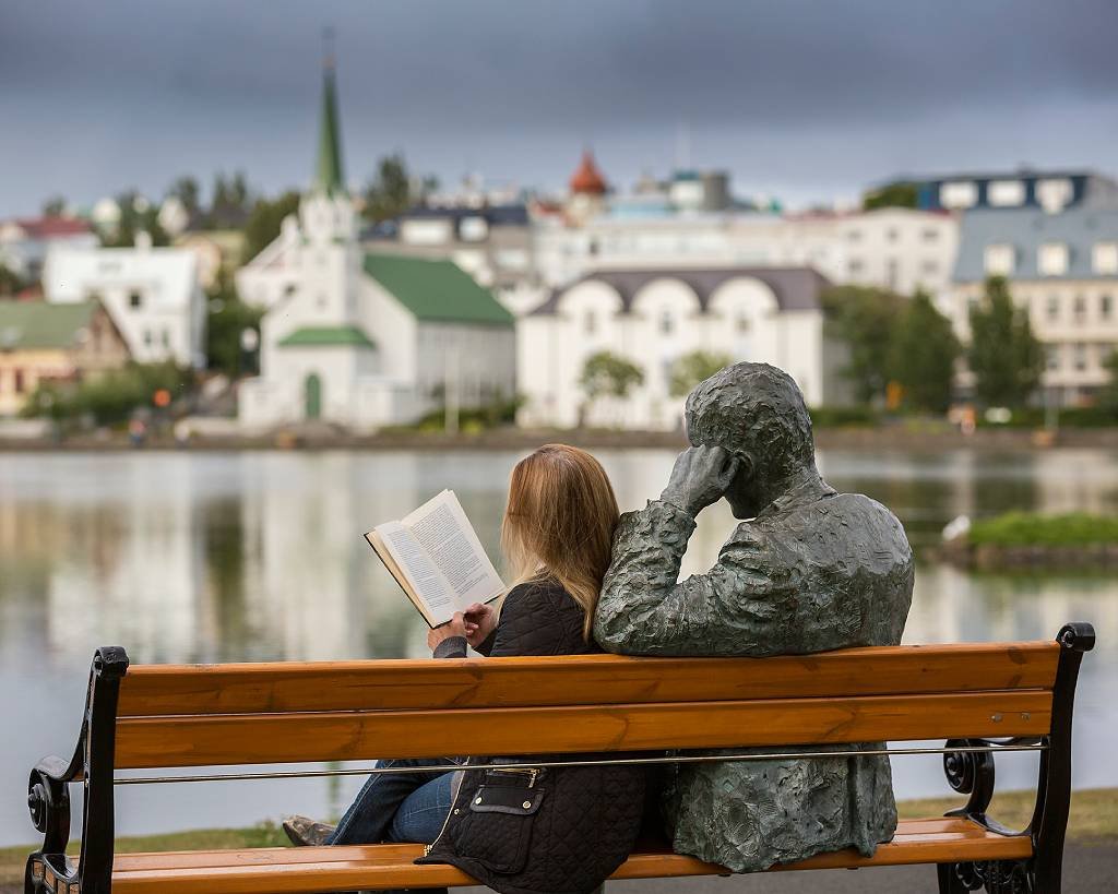 Mulher lendo ao lado de estátua do peta islandês Tomas Gudmundsson em Reykjavik, Islandia.