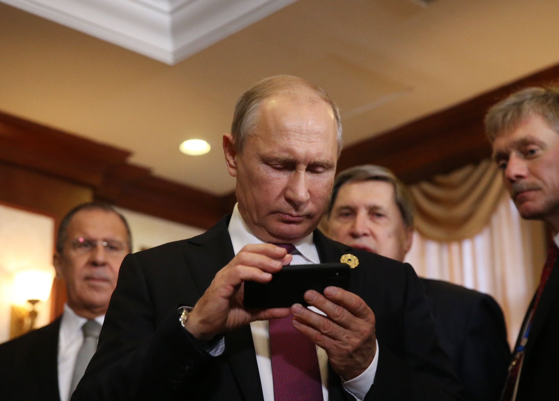 Vladimir Putin examines an iPhone in the company of spokesman Dmitri Peskov (right) and Foreign Minister Sergei Lavrov (left)