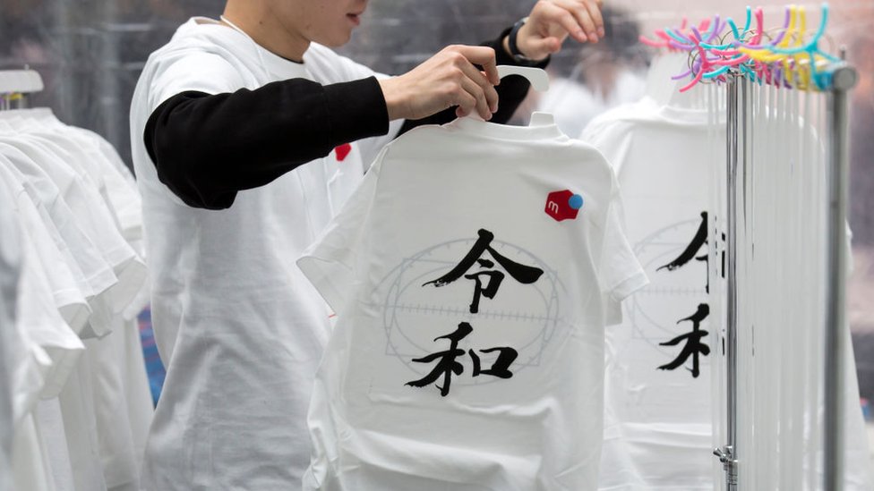 Un empleado cuelga las camisetas con los caracteres de Reiwa