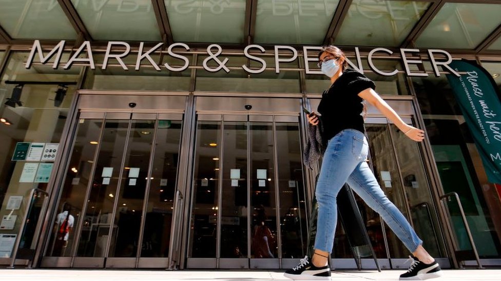 Woman walks by M&S store wearing a face mask