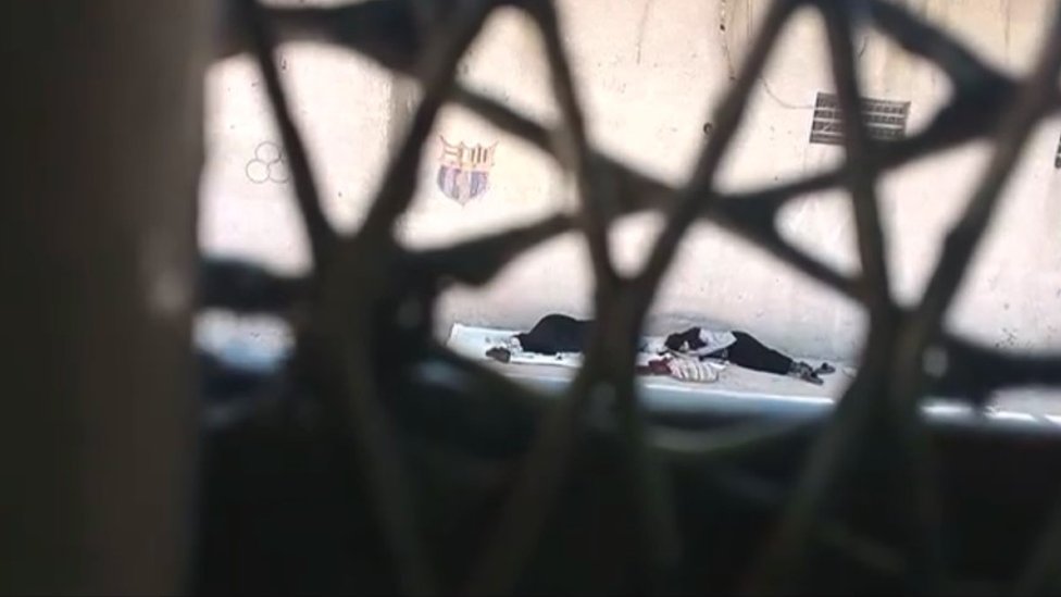 Women lying on the ground seen through a barred window