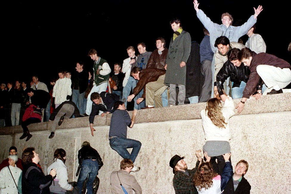 East German citizens climb the Berlin wall at the Brandenburg gate after the opening of the East German border was announced in Berlin on 9 November 1989