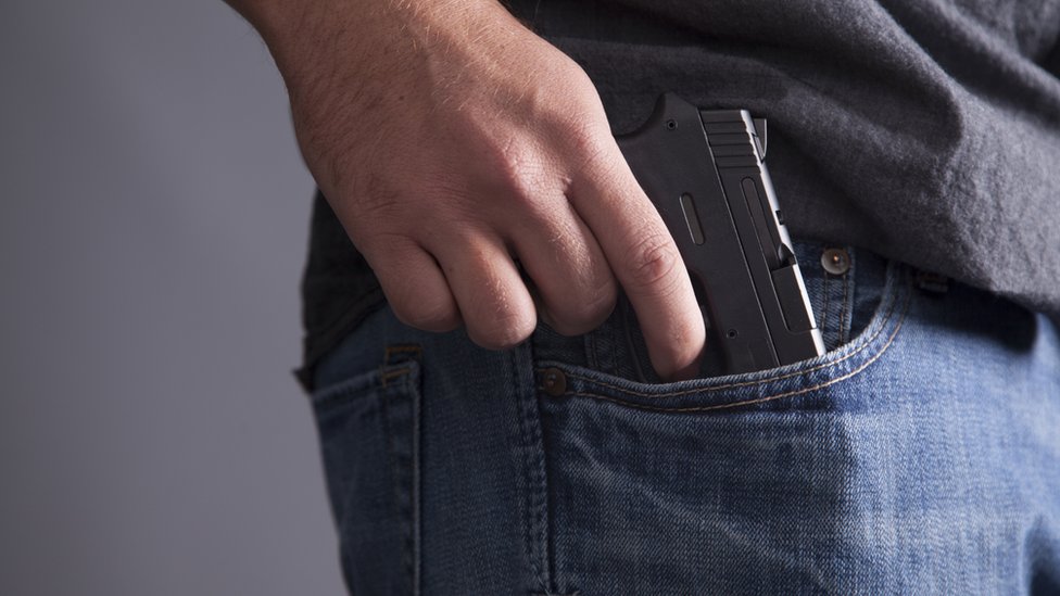 Человек прячет пистолет в кармане
