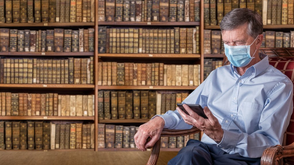 Hombre leyendo en tableta en una biblioteca antigua