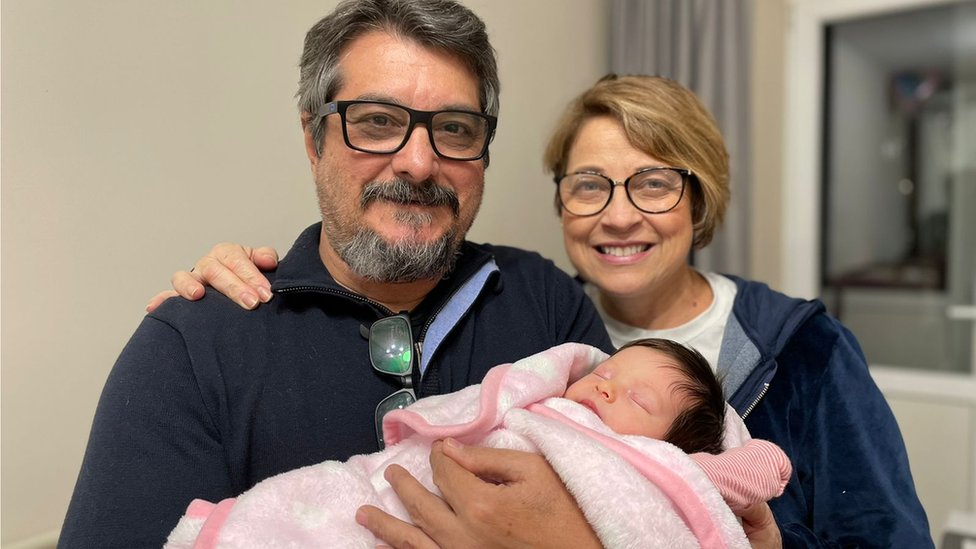 O casal de brasileiros segura a neta recém-nascida