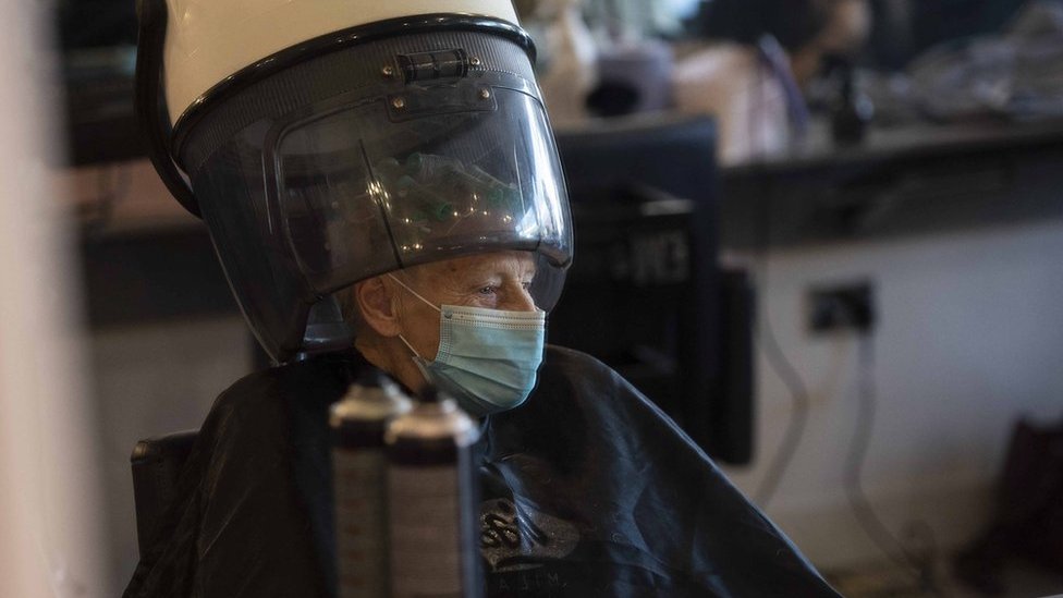 An elderly woman wearing a mask in a hair salon